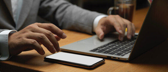 Businessman hand working with smartphone and laptop in office room
