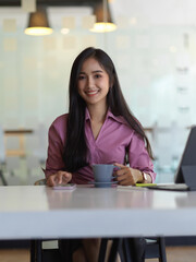 Obraz premium Businesswoman using smartphone and holding coffee cup on worktable