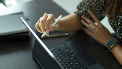 Female hand holding stylus pen to work with digital tablet on worktable