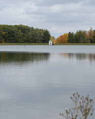 a vertically oriented shot of a small lake house from the far side of the lake with the new england autumn tree line in the background