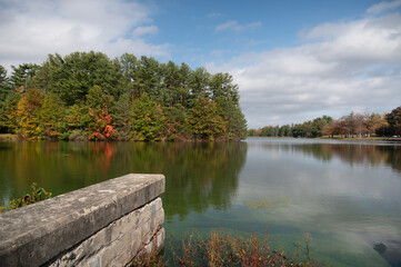 the blue sky and colorful autumn leaves reflect onto a lake in New England on a bright day