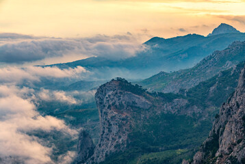 Obraz premium A majestic view of the rocky mountains and the valley in fog and clouds. Creamy fog covered the mountain valley in sunset light. Picturesque and gorgeous scene. Misty sunset over Crimea Mountains