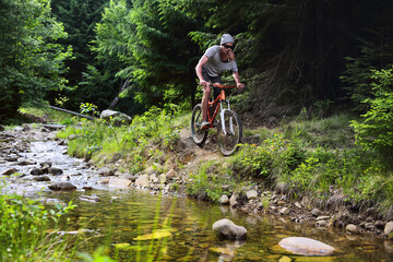 Naklejka premium Young male cyclist riding in the mountain forest against the background of mountain fir trees at sunset.