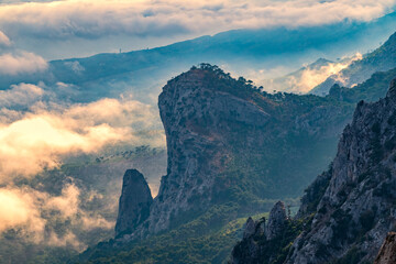 Fototapeta na wymiar A majestic view of the rocky mountains and the valley in fog and clouds. Creamy fog covered the mountain valley in sunset light. Picturesque and gorgeous scene. Misty sunset over Crimea Mountains