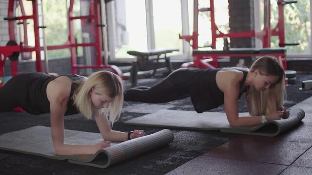 Two fit blonde women does dinamic plank exercise at gym
