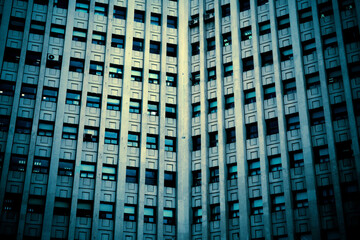 A tall building with some air conditioners hanging outside the window. Toned image.