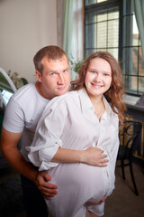 Cute couple including a pregnant woman and a caring man in the living room together
