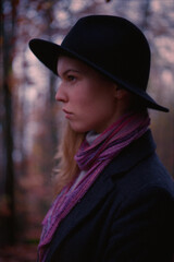 Young Caucasian woman in a black coat and hat in the autumn forest in the mountains. Real grain scanned film.