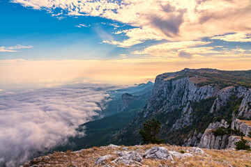Majestic orange sunset over the rocky mountains and the valley in fog and clouds. Creamy fog covered the mountain valley in sunset light. Misty sunset over Crimea Mountains