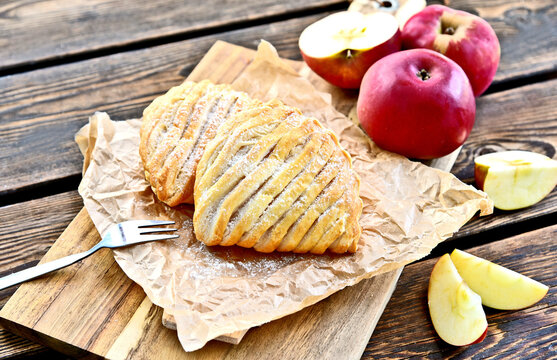 Easy Apple Turnovers (German name is Apfeltaschen) on brown paper with fresh red apples on wooden board and wooden floor.