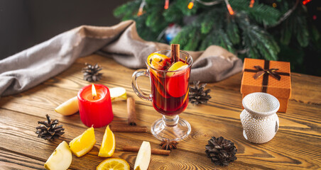 Cup of aromatic hot mulled wine on a wooden table on the background of a Christmas tree with lights. Concept of a festive atmosphere