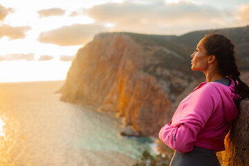 Back view of woman sitting on a mountain top admires the  rising sun over the sea or ocen and...