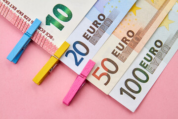 10, 20, 50, 100 Euro banknotes with decorative clothespins on pink background