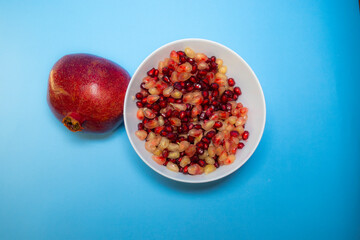 Fresh pomegranate seeds on plate with blue background
