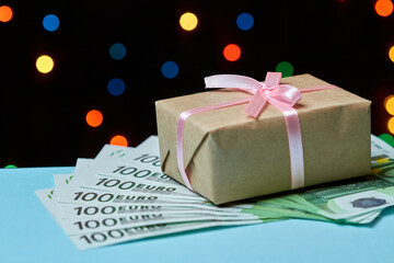 Christmas or New Year gift box on euros against a background of colorful lights. Money as a gift...