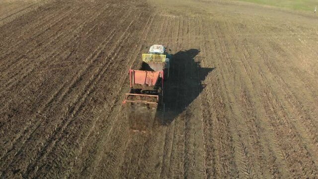 Aerial view of a dirty tractor with a manure spreader on an autumn field. An agricultural machine applies organic fertilizers to brown soil to increase future yields and farmland fertility