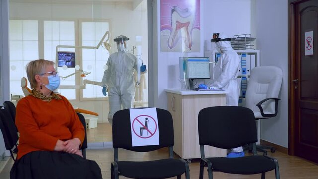 Slow motion of patients with protection mask waiting in crowded stomatology reception with new normal, staff wearing ppe suit. Concept of new normal dentist visit in coronavirus outbreak.