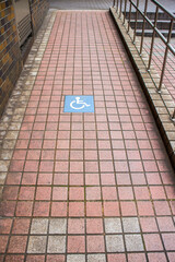 Red tiled ramp way with steel handrail and a wheelchair ramp sign on the floor. 