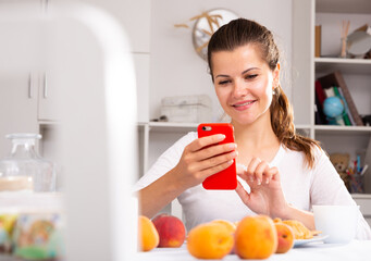 Portrait of young woman housewife using phone at home kitchen