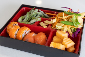 Bento box with California rolls, salad, fruits and Edamame