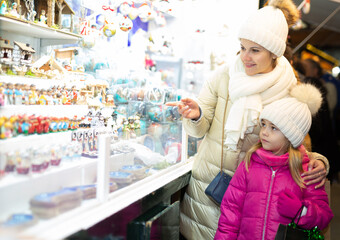 Little girl with happy mom buying figures and workpiece for creating Christmas scenes. High quality photo