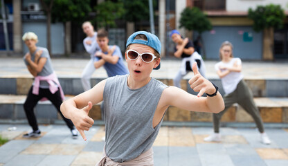 Portrait of modern teenager performing street dance with group of friends outside in summer.