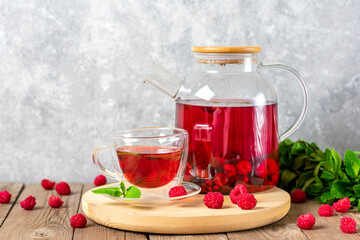 Herbal tea with berries, raspberries, mint leaves and hibiscus flowers in glass teapot and cup on wooden table Medicine for cold Vitamin drink Rustic style