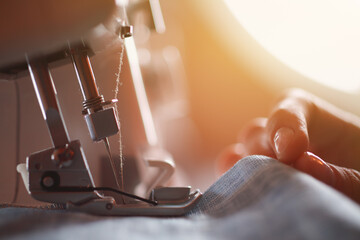 Close-up of woman seamstress hands behind a sewing machine indoors near the window. Close-up of a tailor near a sewing machine.