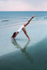 Young caucasian woman doing yoga in sea water on the coast.