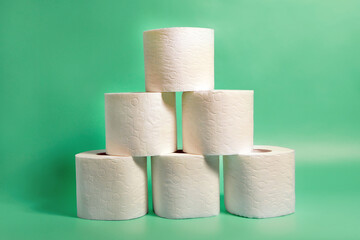 Rolls of white toilet paper pilled up in pyramid on turquoise background.