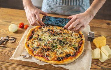 Female chef blogger takes photos of home-made pizza on her phone. The concept of food photography for social networks