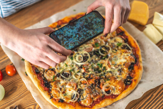 Female chef blogger takes photos of home-made pizza on her phone. The concept of food photography for social networks