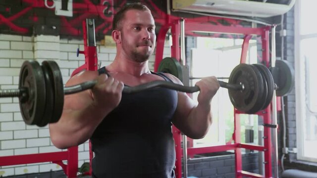 Close up of an attractive man bodybuilder performing barbell biceps curls
