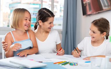 Happy mother teaches her daughters to draw at home