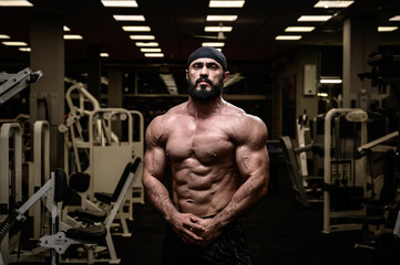 Fototapeta na wymiar strong bearded athlete in bandana posing in dark gym