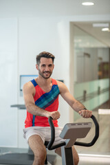 Plakat Young man in bright tshirt exercising on a gym machine and smiling
