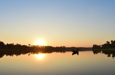 A man spread his net to catch fish and waiting , the sun is yellowish in color .