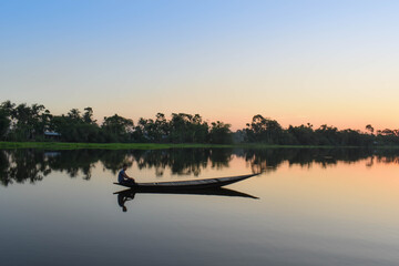 A man spread his net to catch fish and waiting , the sun is yellowish in color .
