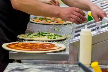 Cook in the kitchen putting the ingredients on the pizza. Production and delivery of food.