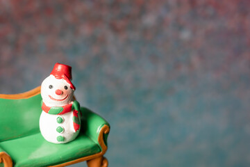 A snowman model sitting on a green sofa with a blurry bokeh background