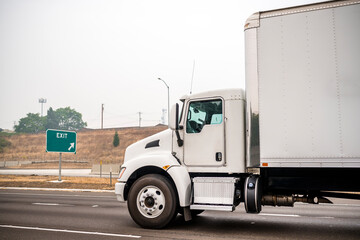 Powerful day cab big rig semi truck with box trailer delivering cargo running on the highway road with fire smog