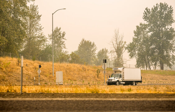 Small Rig Semi Truck With Refrigerated Box Trailer Transporting Cargo Running On The Road In Smoke And Smog From A Forest Fire