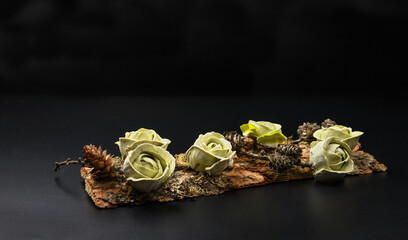 A fragment of tree bark with delicate marshmallow roses of a soft green color on a black background.