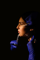 Fototapeta premium Attractive young woman gets cosmetic injection, isolated over black background. Doctors hands making an injection in face. Beauty Treatment.