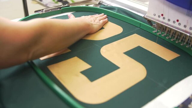 Seamstress adjusts golden number on fabric before embroidery