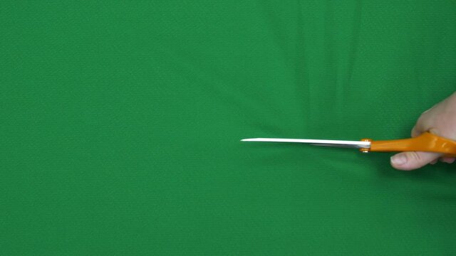 Dressmaker cuts bright green fabric with scissors at table