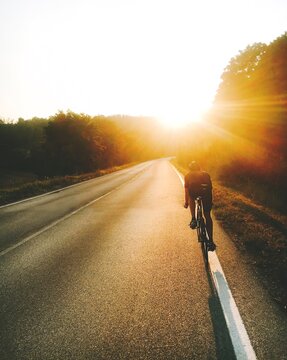 Rear View Of Person Cycling On Road Against Sky During Sunset