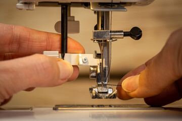 Woman's fingers putting thread in needle loop on electric modern sewing machine for start sewing. Steel needle with looper and presser foot. Close up view of female working hands.