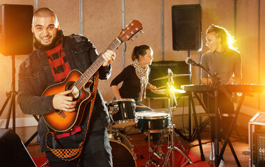 Obraz premium Rehearsal of music band. Glad happy guy guitar player and singer practicing with band members in recording studio
