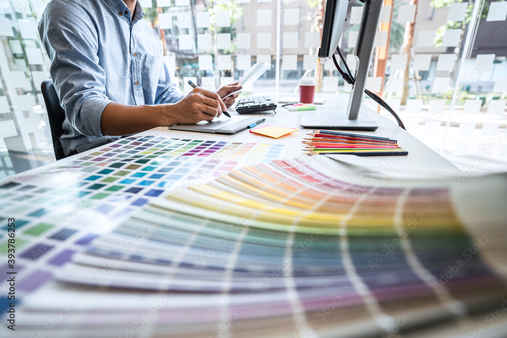 Poster Image of male creative graphic designer working on color selection and drawing on graphics tablet at workplace with work tools and accessories in workspace